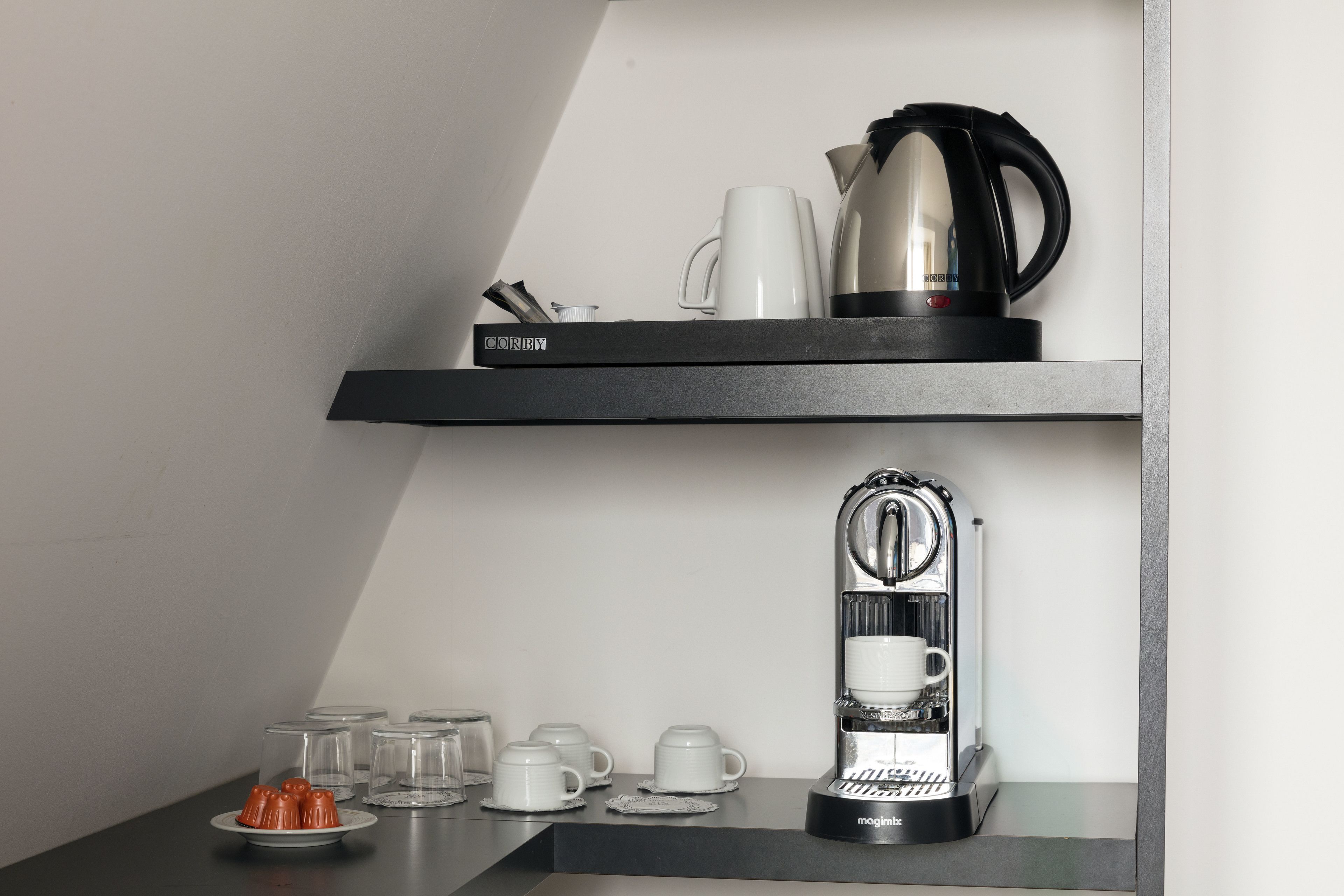 Un área de cocina con cafetera, hervidor y repisa con tazas y una taza.