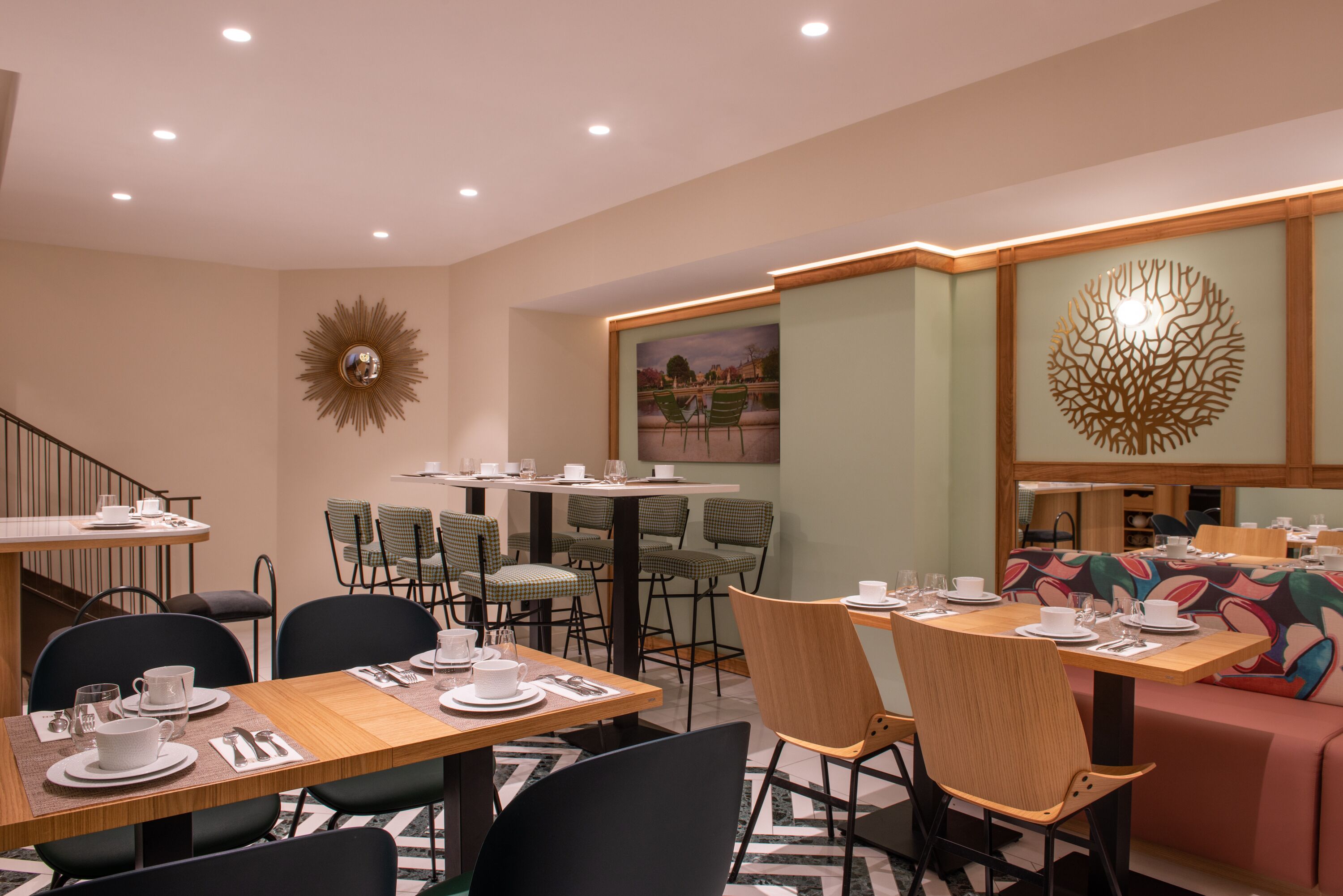 Un espace repas avec des tables préparées pour deux personnes, des chaises et un escalier menant à un niveau supérieur.