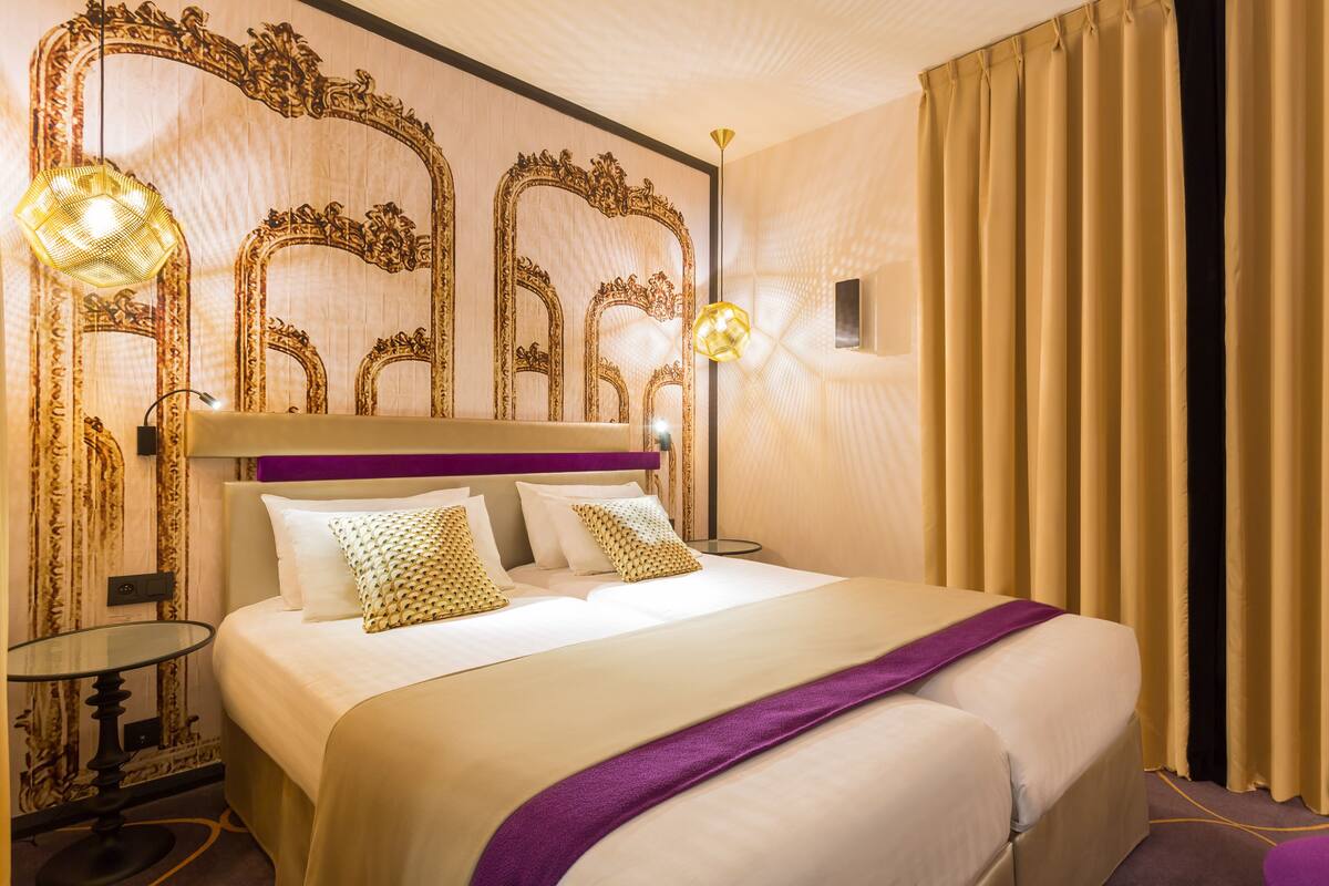 A hotel room with a large bed, ornate wall mirrors, and a purple headboard.