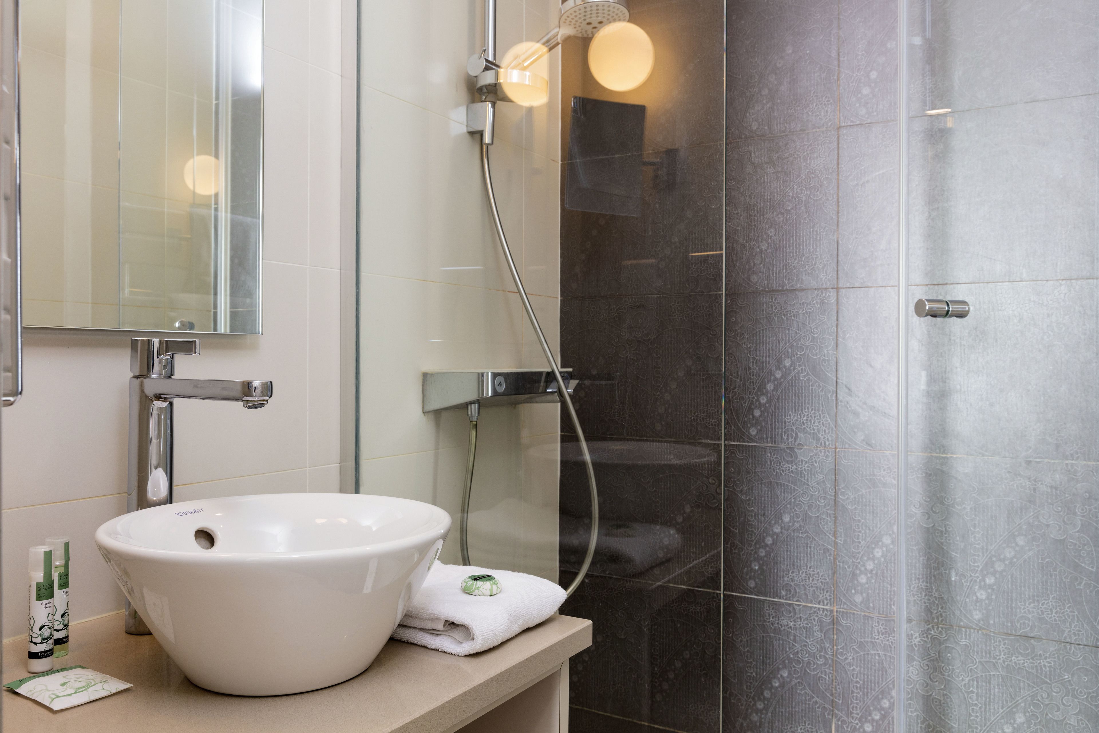 Un bagno con un lavandino bianco, uno specchio, una doccia con porta in vetro e un asciugamano sul ripiano.