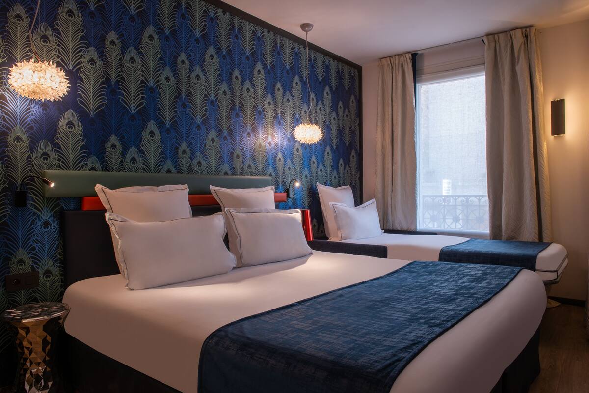 A hotel room with two beds, a large window with curtains, and a decorative wall pattern.