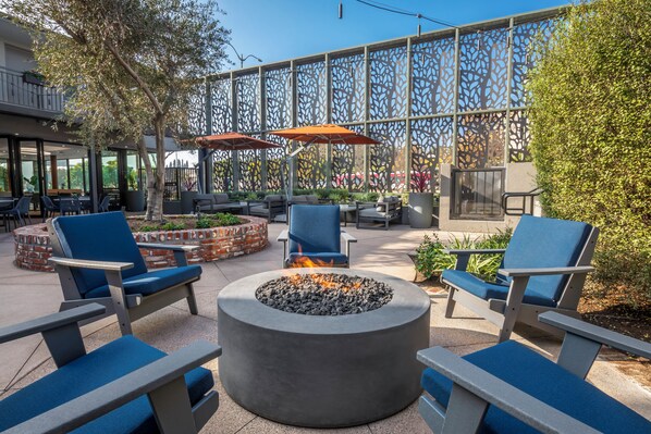 An outdoor seating area with blue chairs and a circular fire pit. - Olivia Hotel (Los Angeles)