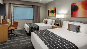 Habitación de hotel con dos camas, un escritorio, una silla y obras de arte en las paredes.