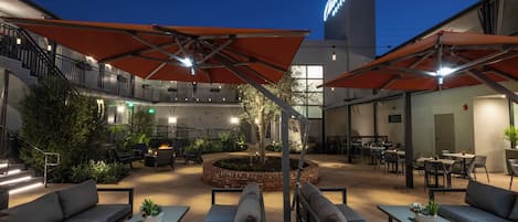 An outdoor patio area with seating, umbrellas, and a central fire feature.