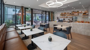 Un café moderno con mesas de mármol, asientos acolchados y una zona de cocina con estantes llenos de aperitivos y bebidas.