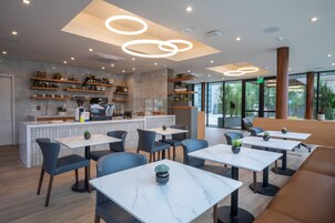 Un restaurante moderno con mesas de mármol, asientos acolchados y una cocina visible al fondo.