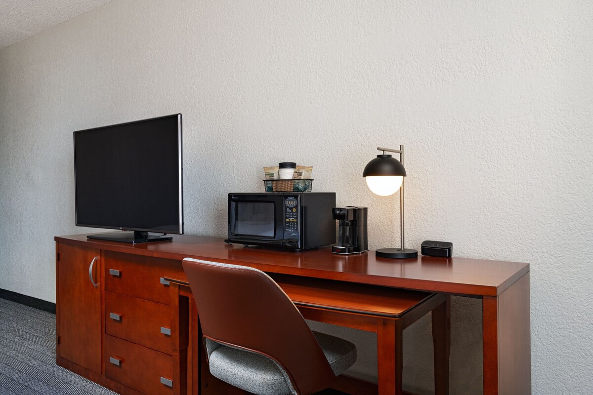 A hotel room with a wooden desk, a television, a microwave, a coffee maker, and a lamp.