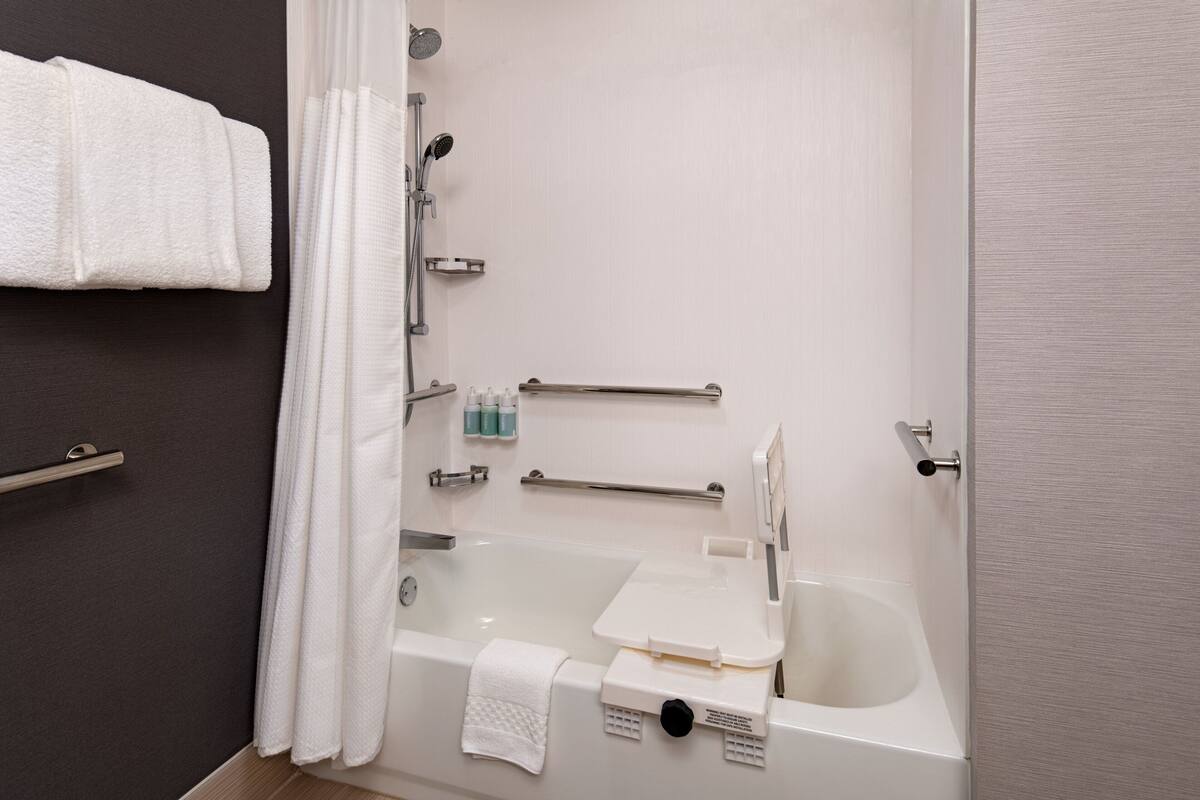 A modern bathroom with a bathtub, shower, and handrails.