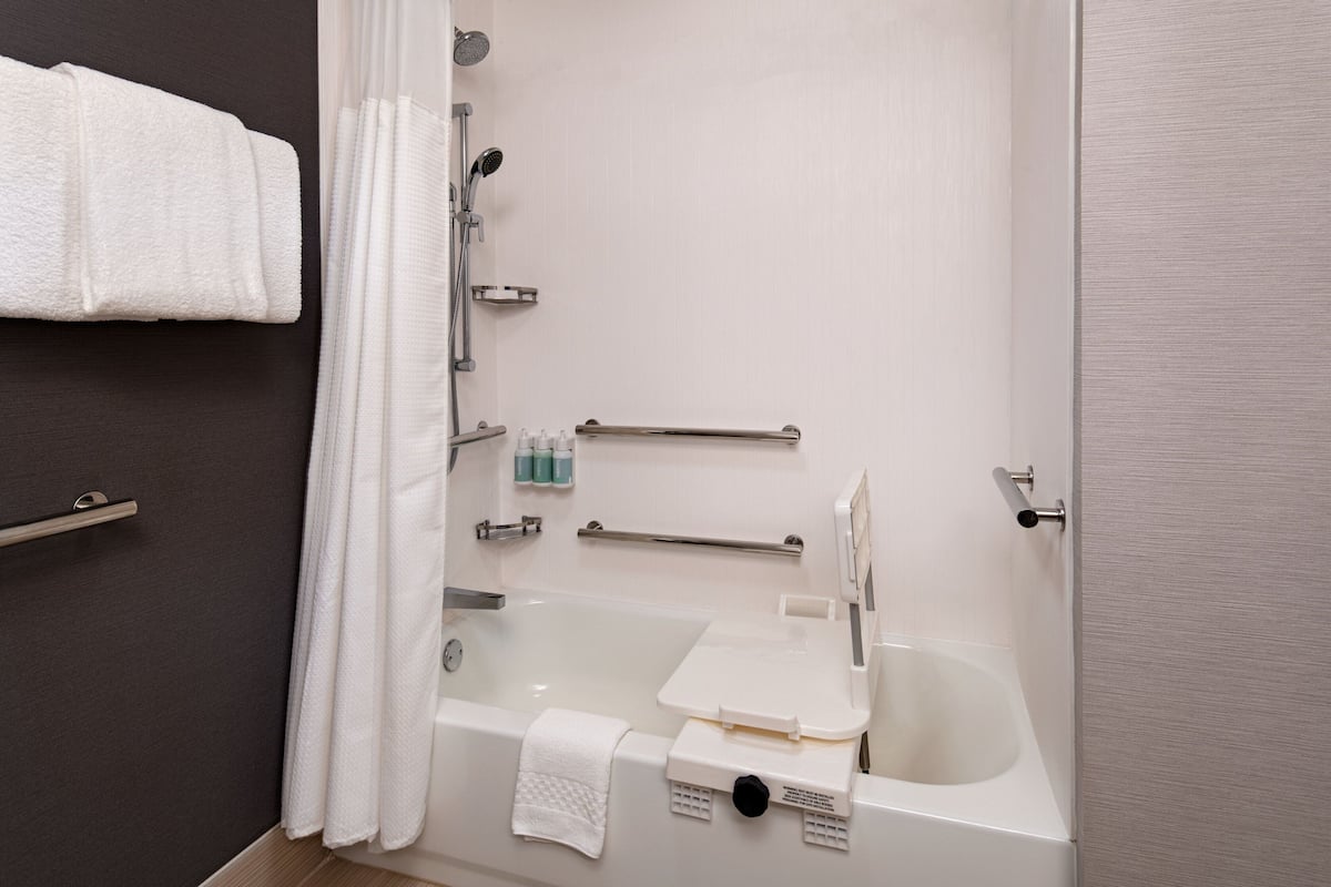A modern bathroom with a bathtub, shower, and handrails.