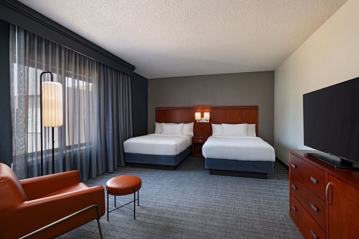 A hotel room with two beds, a TV, a desk, and a chair.