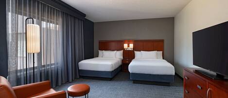 A hotel room with two beds, a TV, a desk, and a chair.