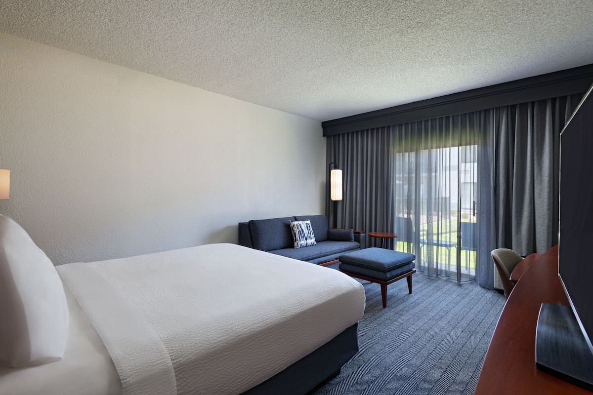 A hotel room with a large bed, a sofa, a small table, and a TV.