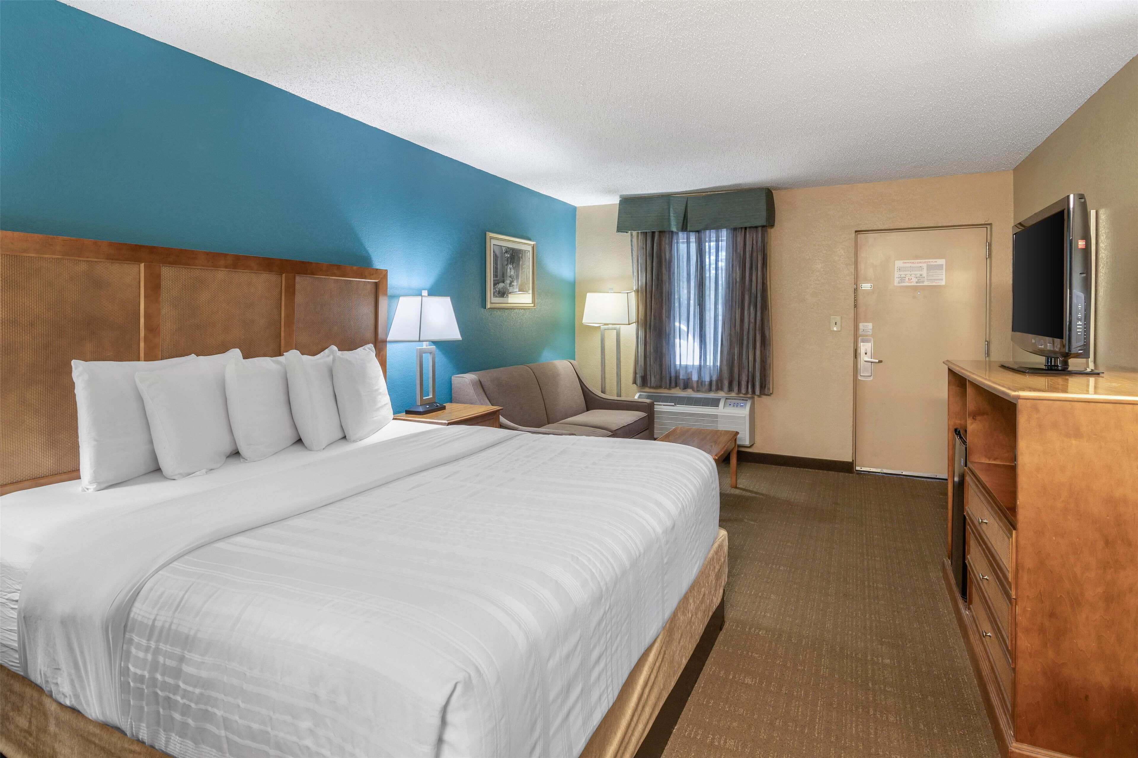 Une chambre d’hôtel avec un grand lit, un bureau avec un ordinateur, une télévision et une fenêtre avec des rideaux.