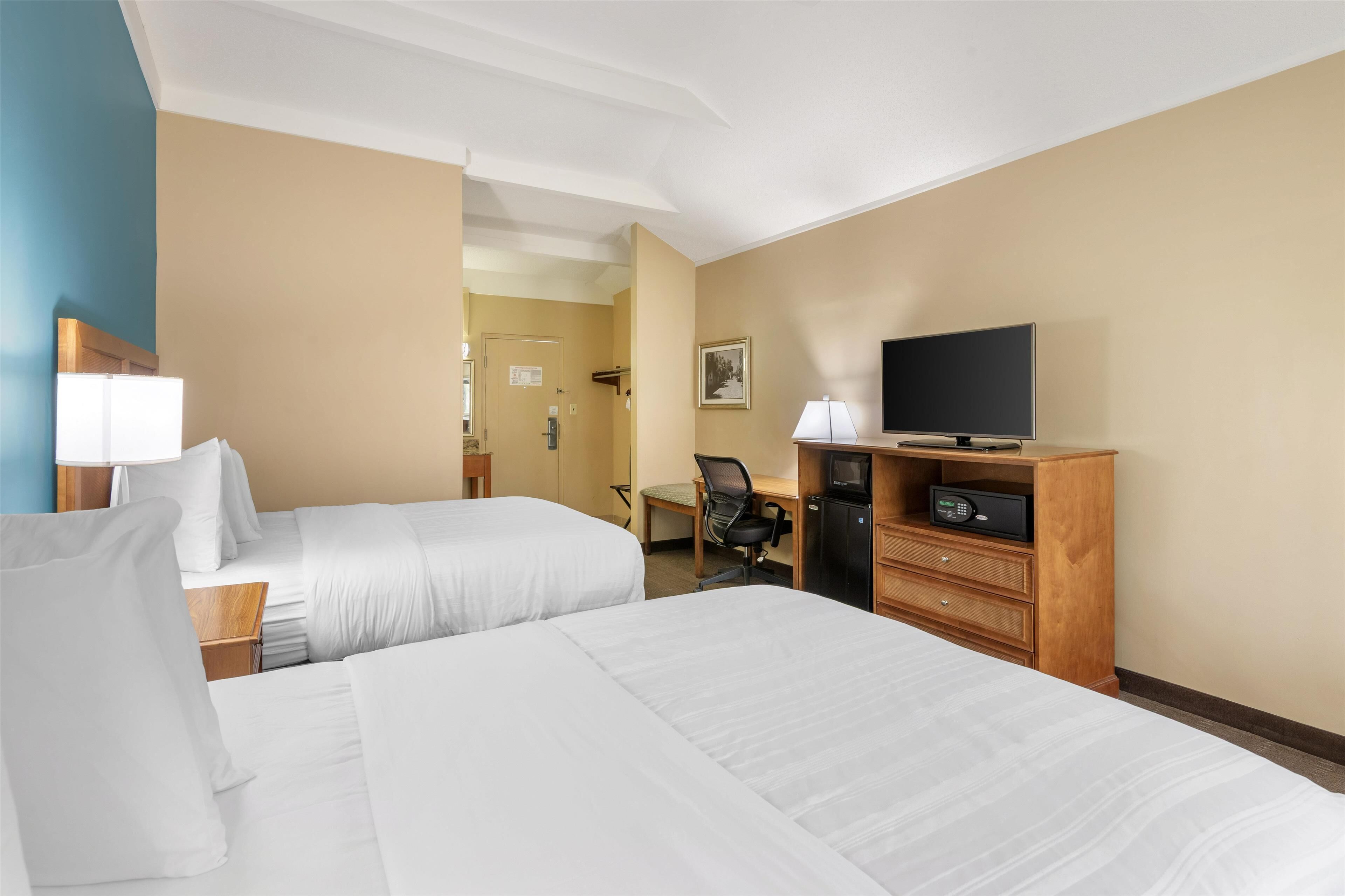 A hotel room with two beds, a desk with a chair, a television, and a minibar.