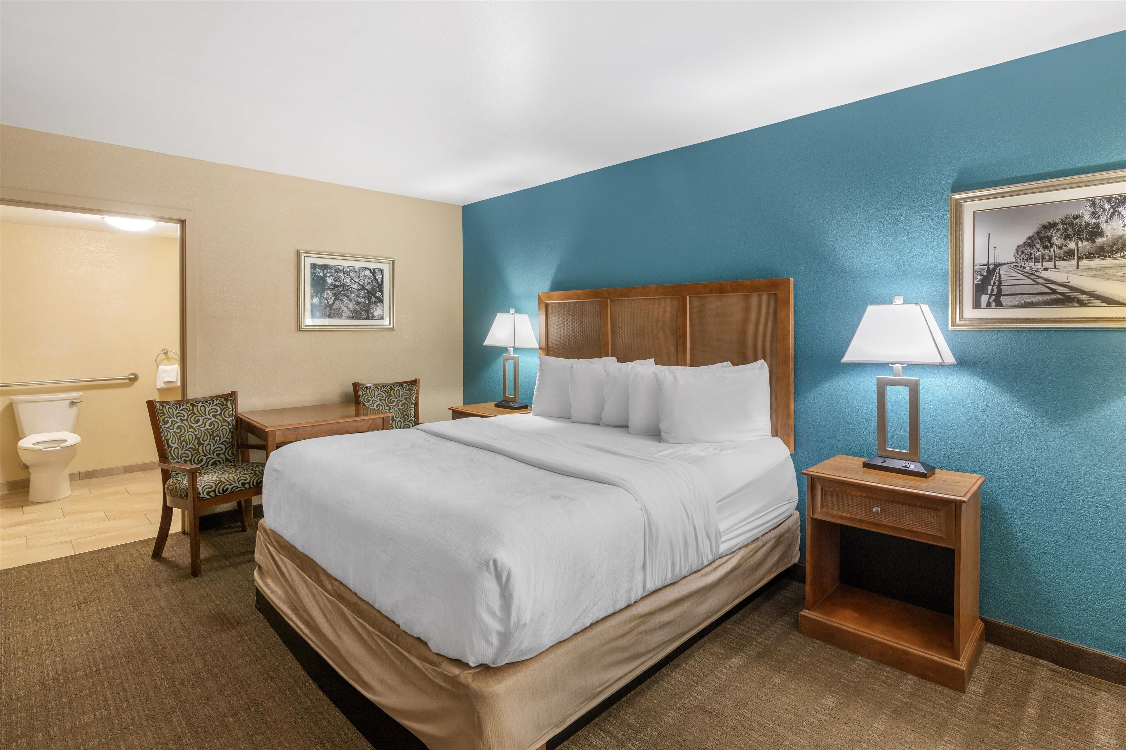 A hotel room with a large bed, two bedside tables with lamps, a chair, and a framed picture on the wall.