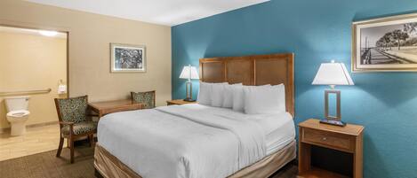 A hotel room with a large bed, two bedside tables with lamps, a chair, and a framed picture on the wall.