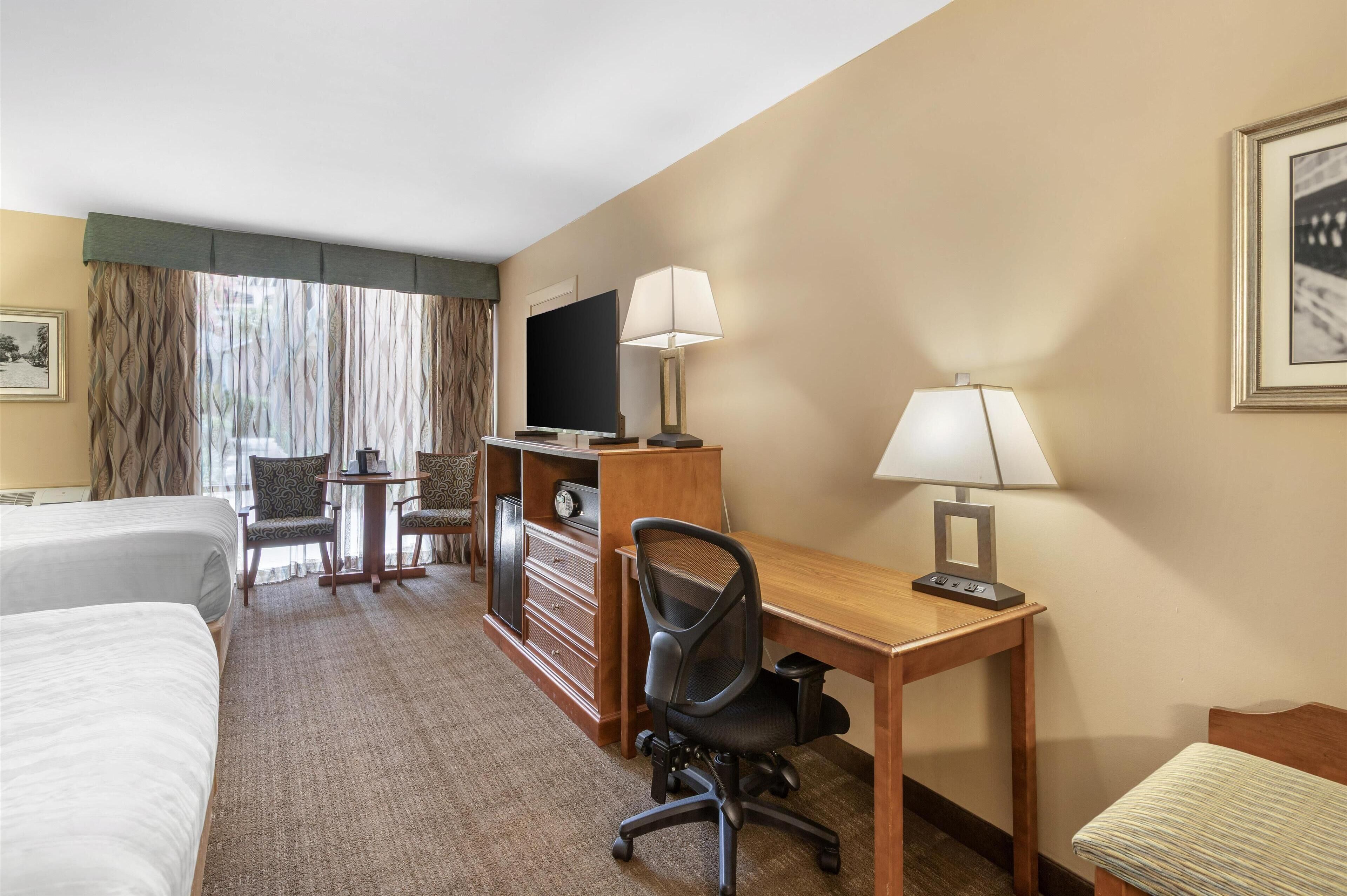 Une chambre d’hôtel avec deux lits, un bureau avec un ordinateur, une télévision et une chaise.