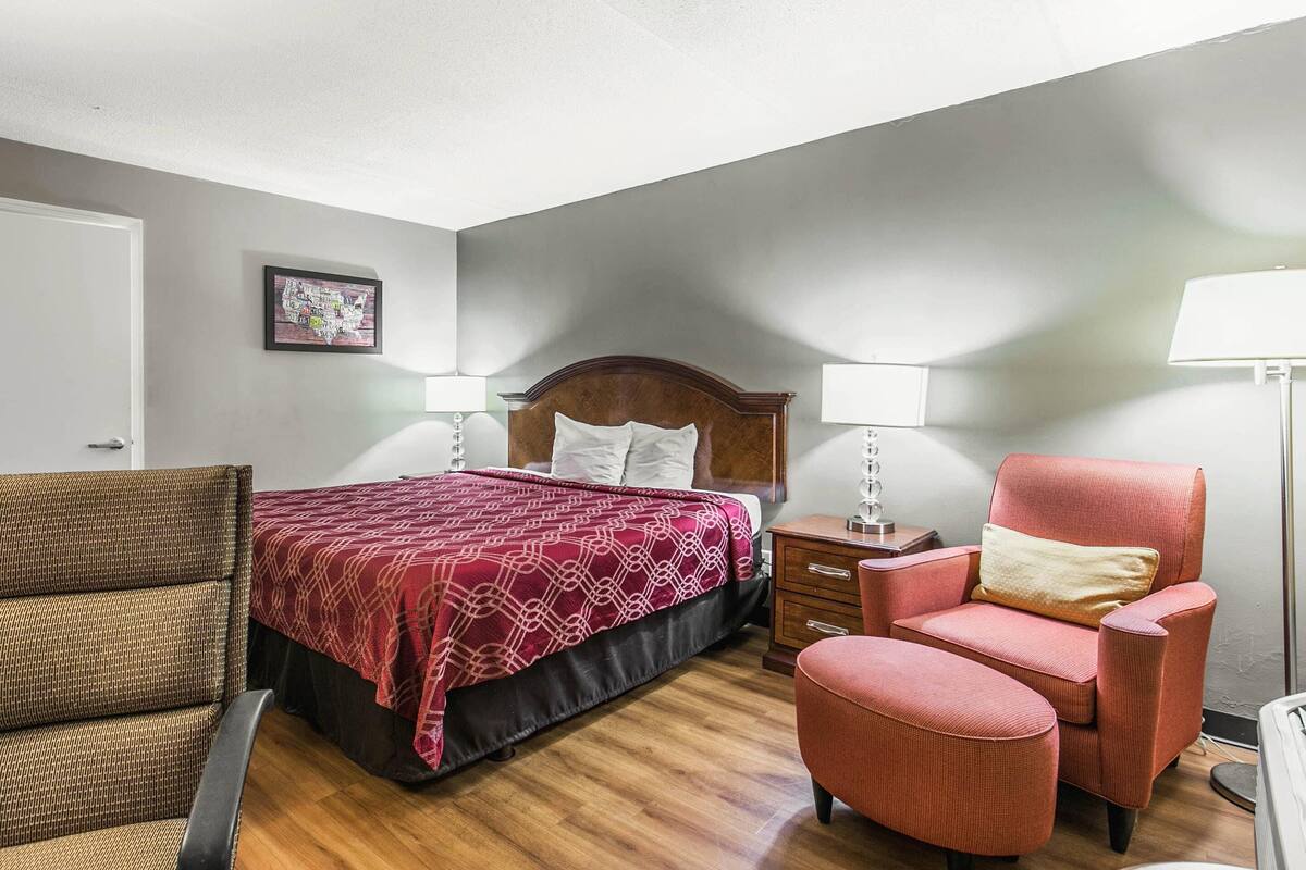 A hotel room with a bed, two chairs, a nightstand, and a bedside table with lamps.