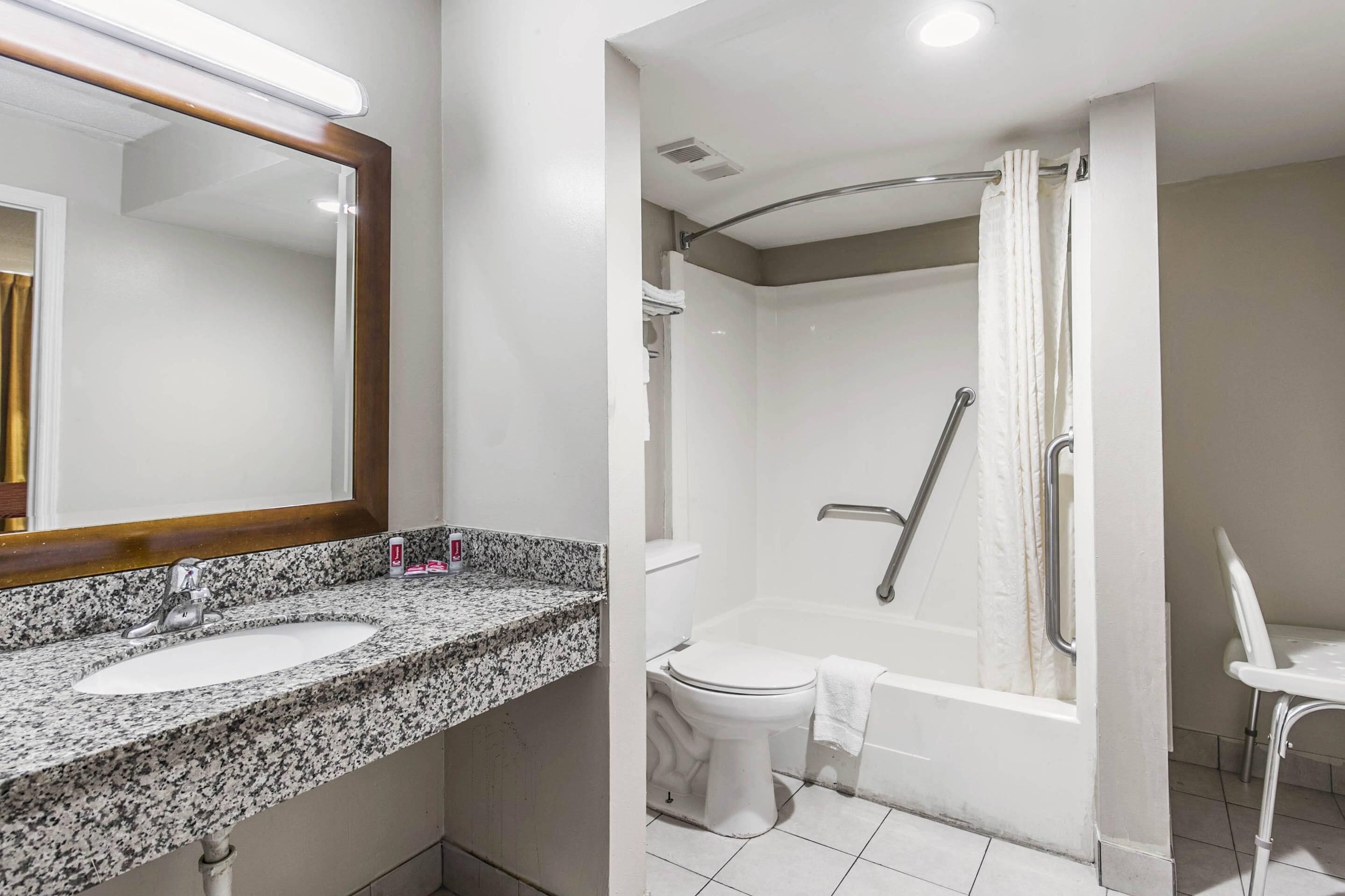 A modern bathroom with a granite countertop sink, a white toilet, and a walk-in shower with a glass door.