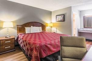 Una habitación de hotel con cama, mesita de noche, lámpara, silla y un cuadro en la pared.