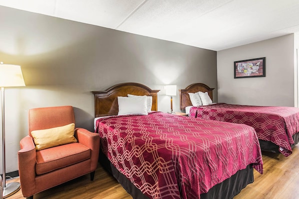 Une chambre d’hôtel avec deux lits simples, une tête de lit en bois, un fauteuil rouge et une lampe sur pied.