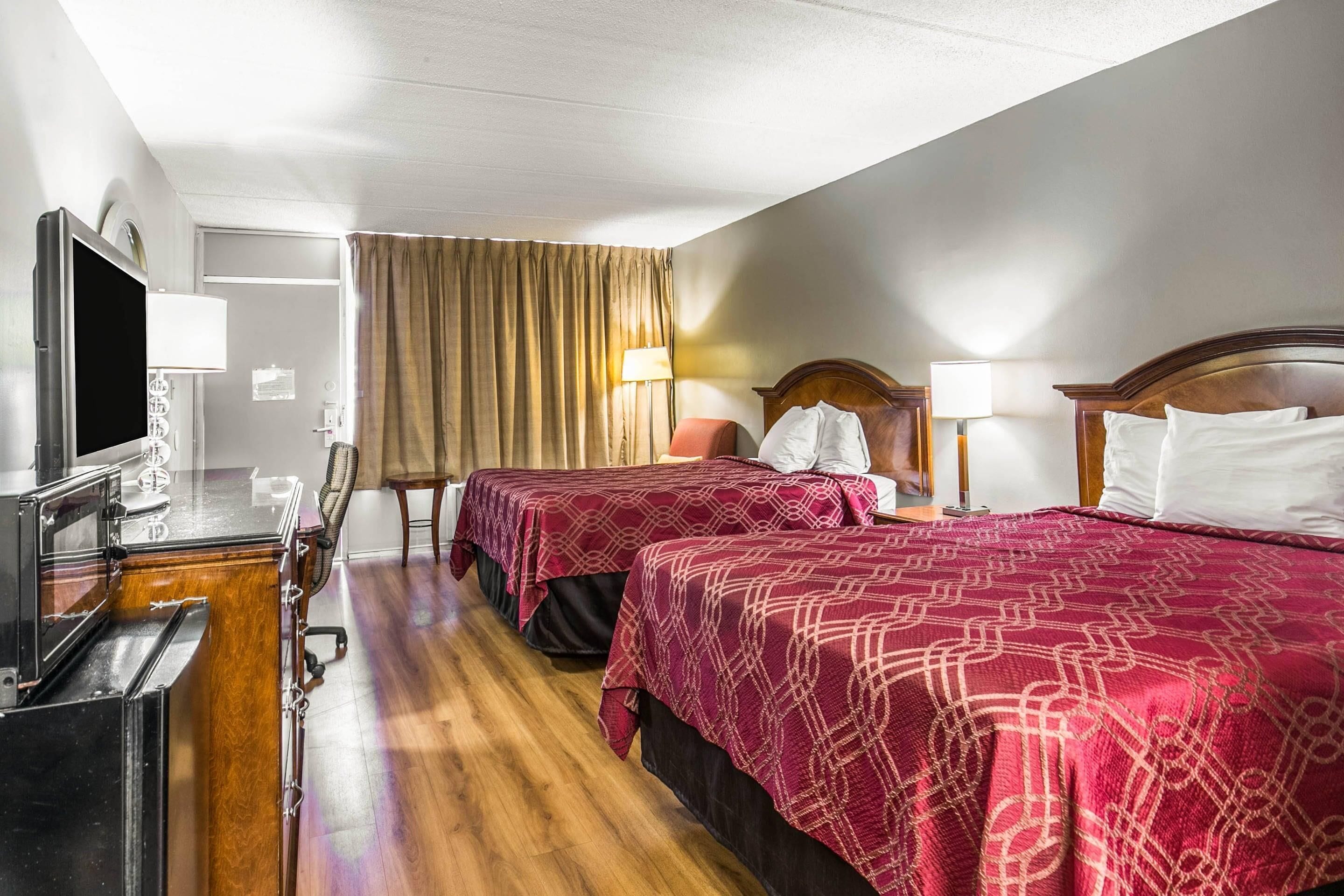 Habitació d'hotel amb dos llits, una taula de treball, una televisió de pantalla plana, una cadira i una làmpada.