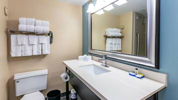 A bathroom with a toilet, sink, and mirror. There are towels hanging on a rack and a trash can.