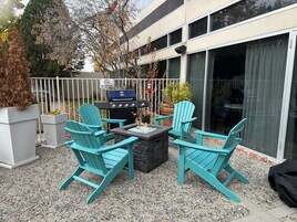 Un patio al aire libre con una parrilla, dos sillas Adirondack y un brasero.