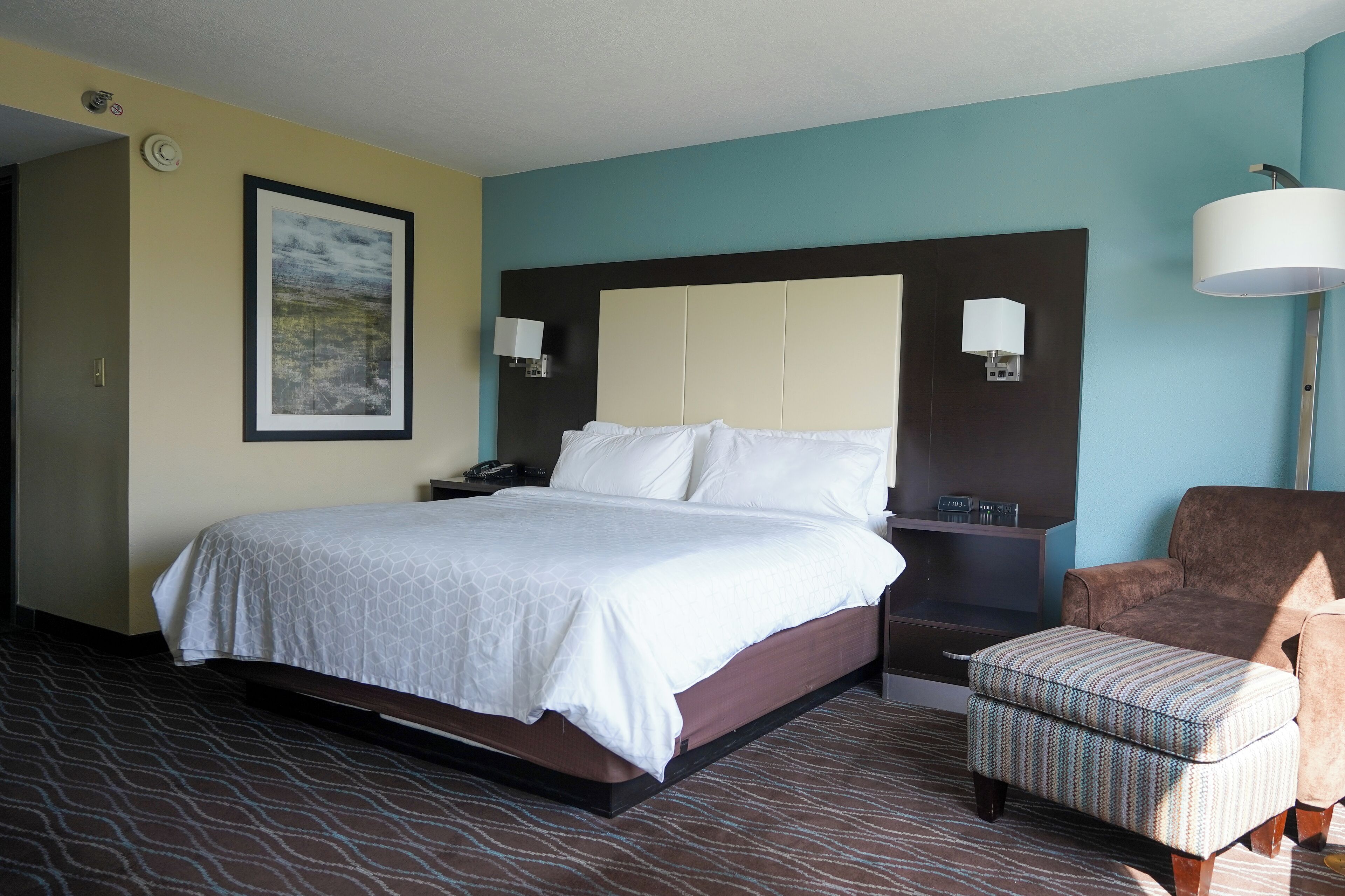 A hotel room with a large bed, two bedside lamps, a chair, and a nightstand.