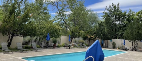 An outdoor swimming pool with lounge chairs and umbrellas, surrounded by trees.
