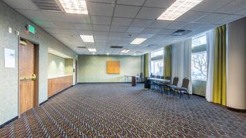 Un salón de conferencias con alfombra estampada, una mesa grande con sillas, un cuadro en la pared y ventanas con cortinas.