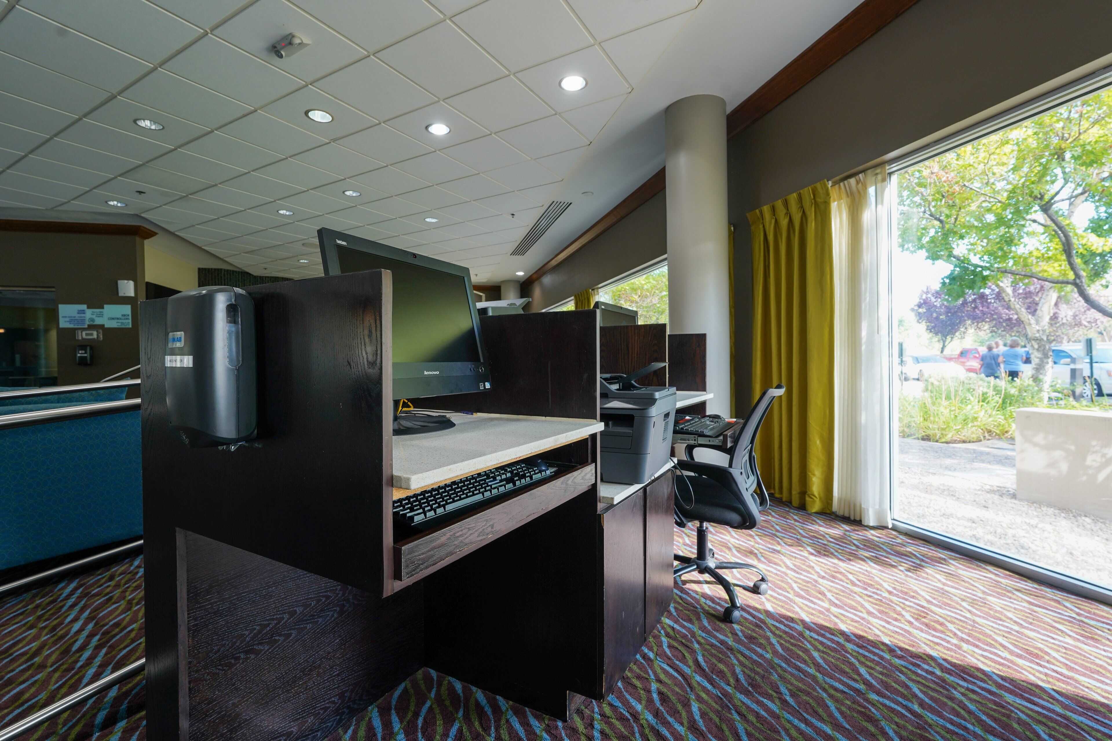 A hotel room with a desk, computer, and a view of the outdoors.