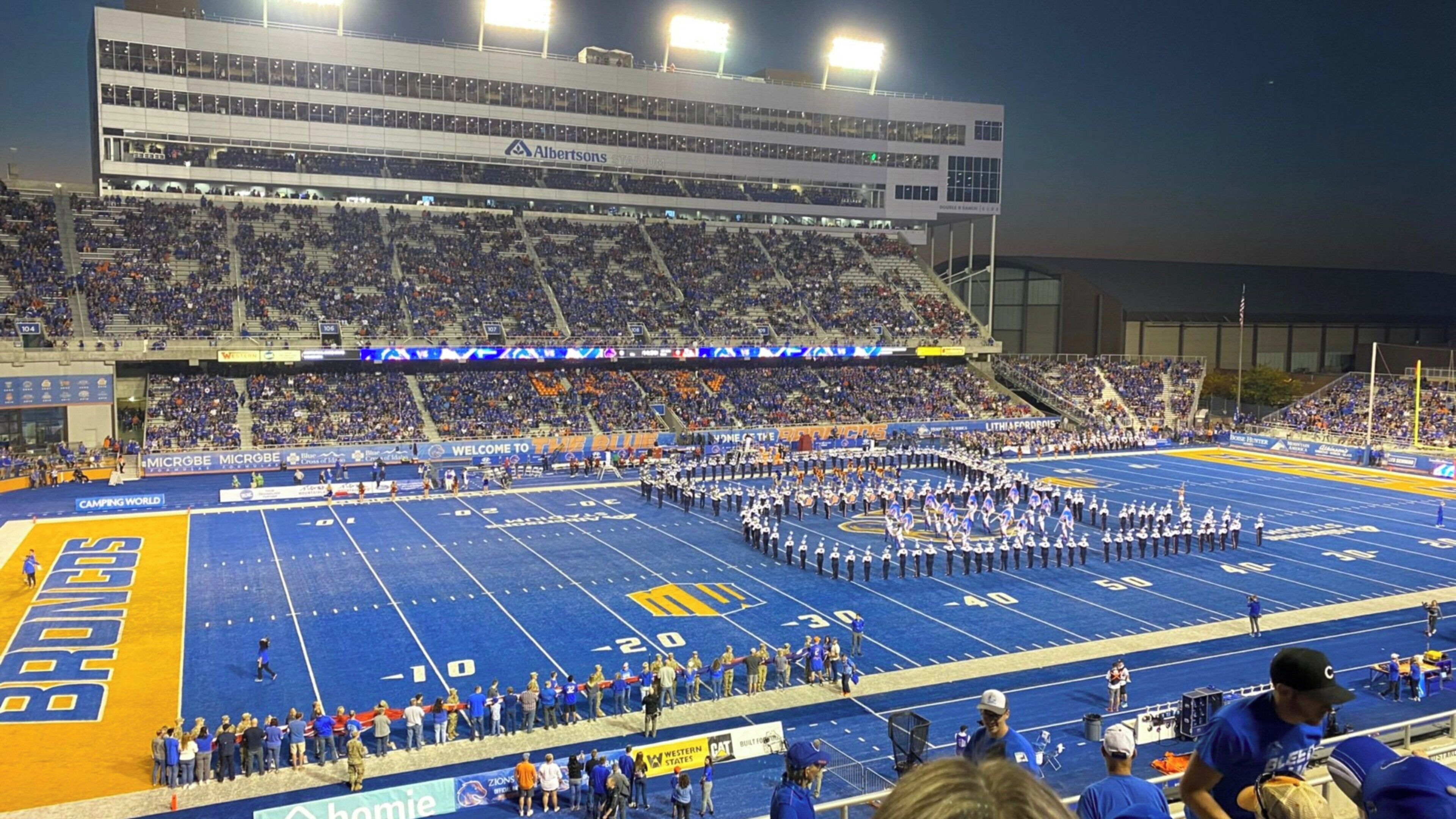 A football stadium with a marching band formation on the field, surrounded by spectators.