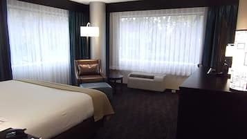 A hotel room with a large bed, a desk, a chair, and a window with curtains.