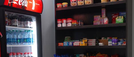 Una máquina expendedora con diversas bebidas y un estante lleno de alimentos como sopa y aperitivos.
