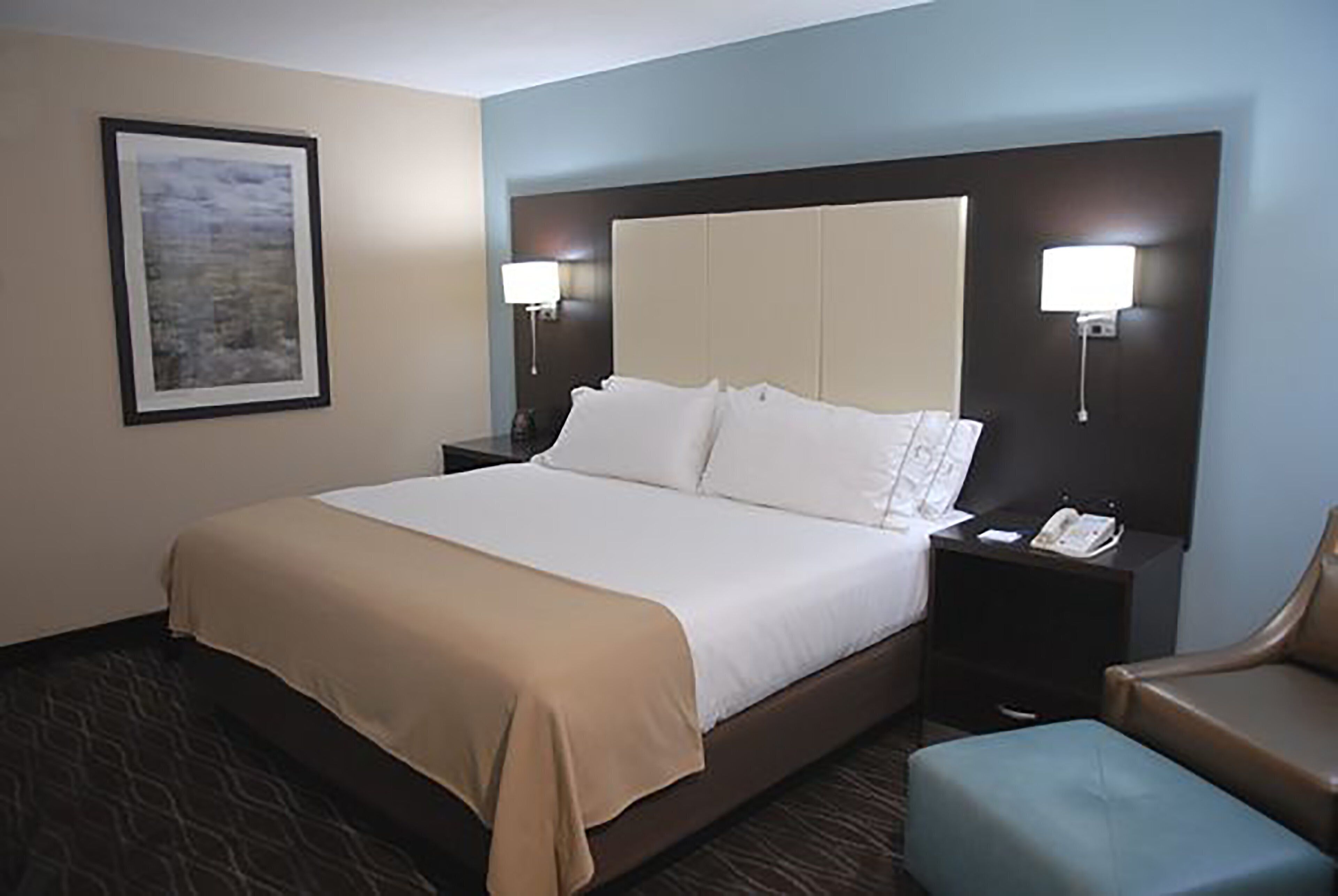 A hotel room with a large bed, two bedside tables, a chair, and a framed picture on the wall.