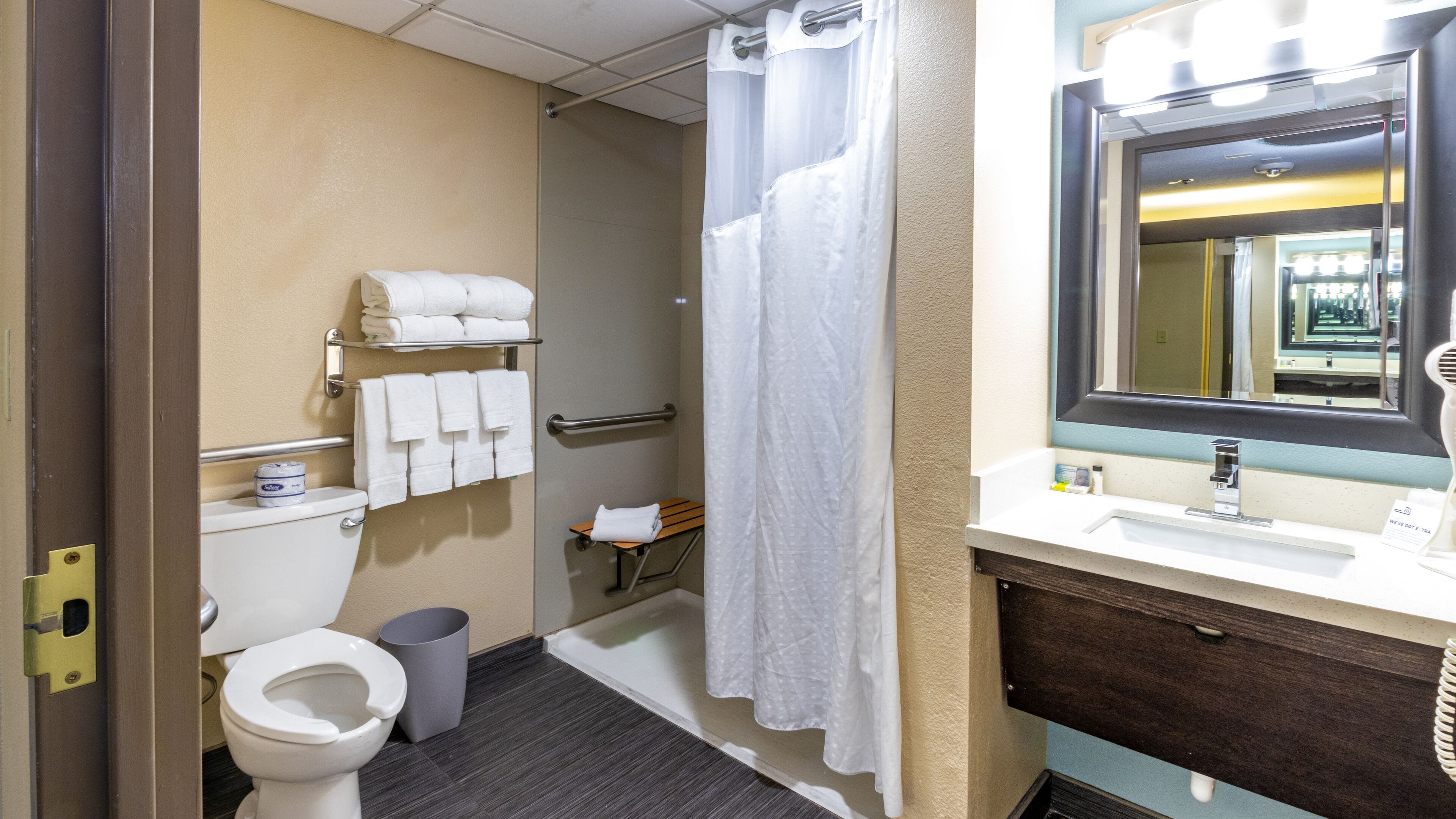 Un baño de hotel con inodoro, lavamanos, espejo, ducha y toallero.