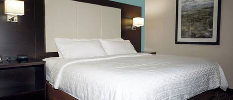A hotel room with a large bed, two bedside tables, a nightstand, and a wall-mounted lamp.