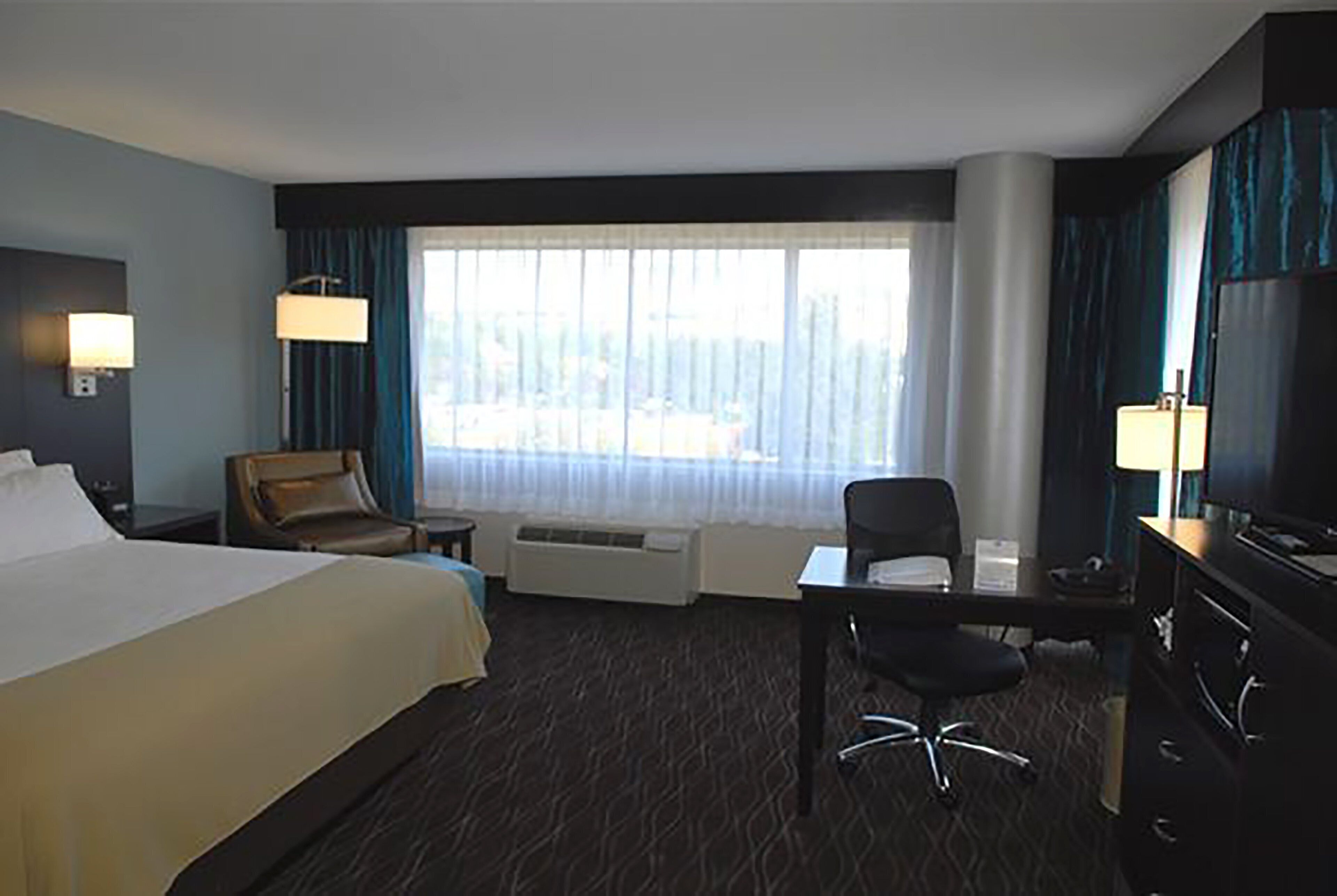 A hotel room with a large bed, a desk with a chair, a television, and a window with curtains.