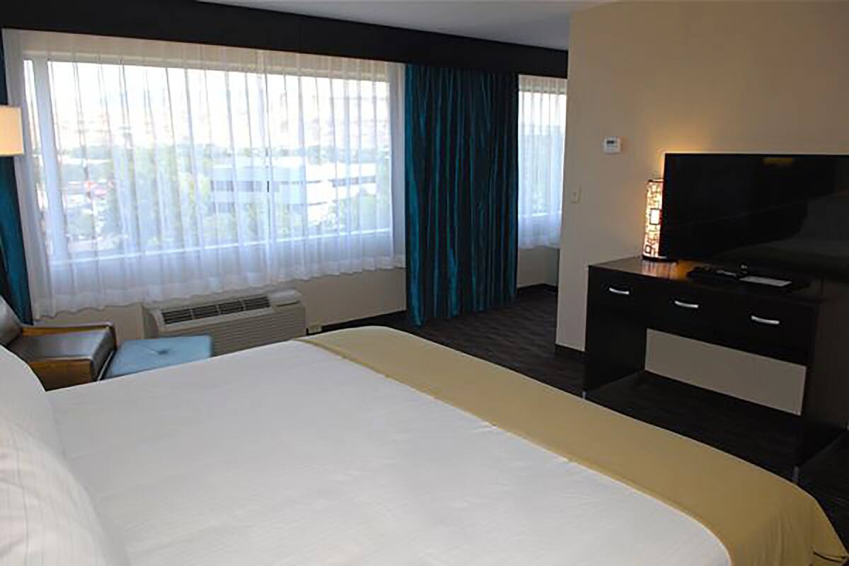 Habitación de hotel con una cama grande, un televisor sobre un mueble, un calentador y una ventana con cortinas.