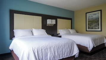 Une chambre d’hôtel avec deux lits, une table de chevet, une lampe fixée au mur et un tableau encadré.