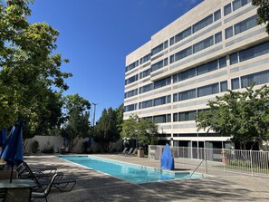 A swimming pool area with lounge chairs and umbrellas, surrounded by trees and a modern building with multiple windows. - Holiday Inn Express Boise - University Area by IHG (Boise)