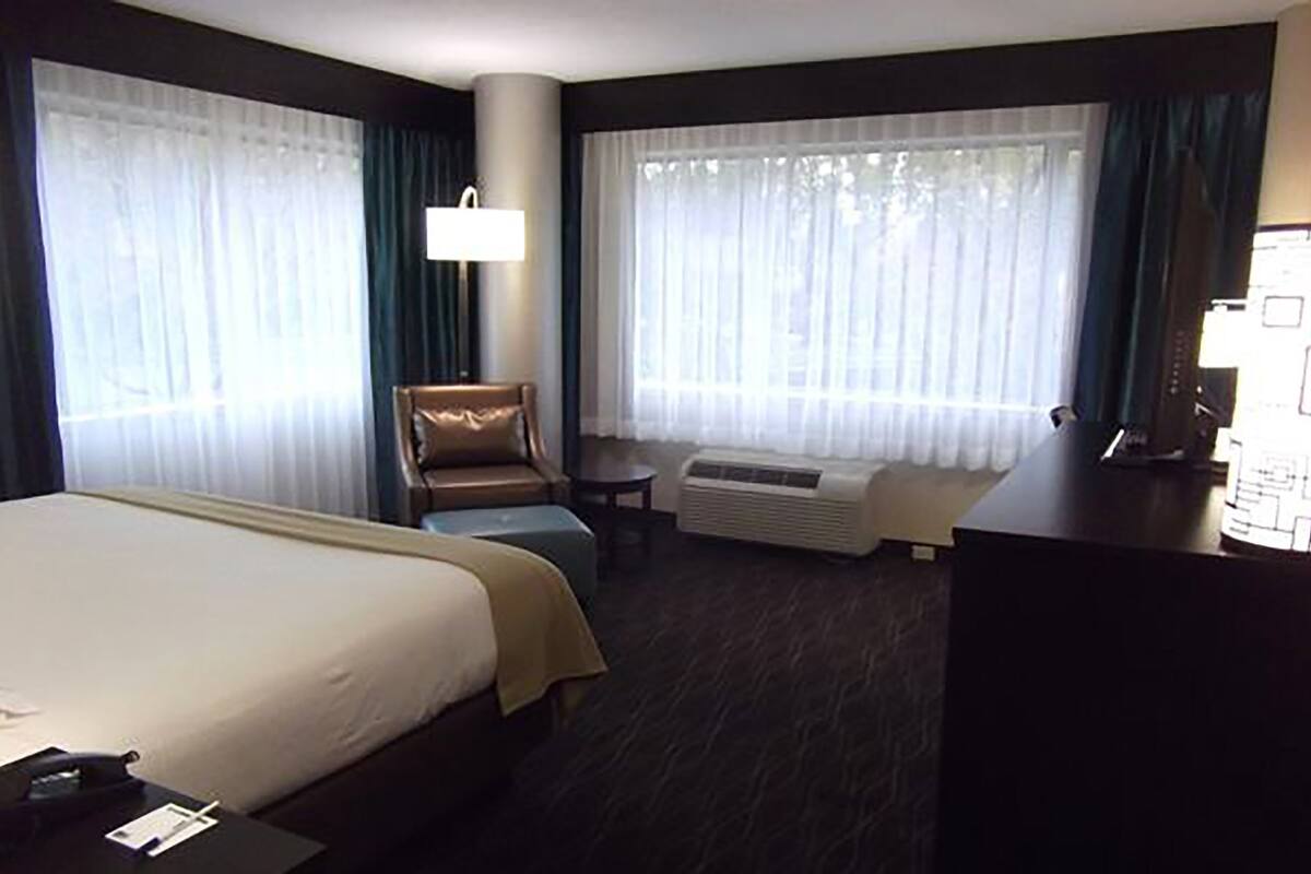 Una habitación de hotel con una cama grande, un escritorio, una silla y una ventana con cortinas.