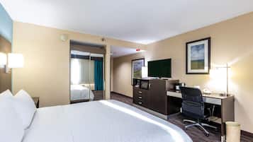 A hotel room with a large bed, a desk with a computer, a chair, a TV, and a mirror.