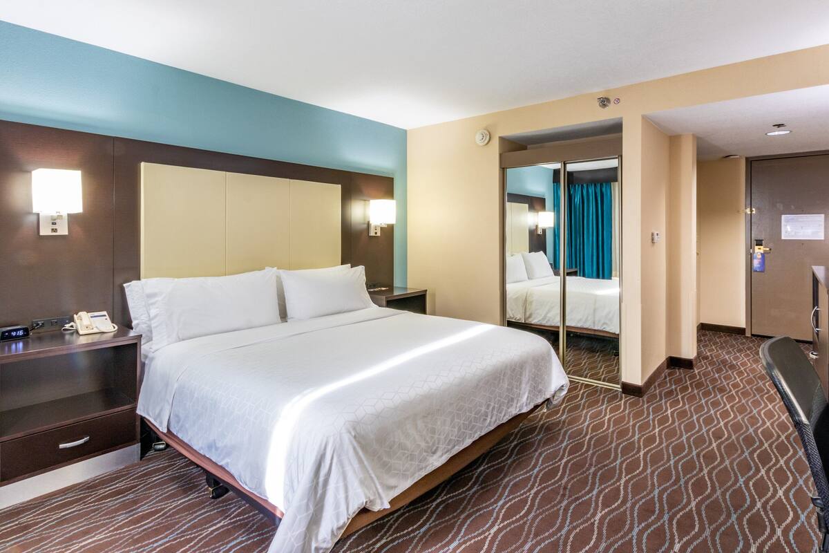 Habitación de hotel con una cama grande, mesitas de noche, un escritorio y un espejo.