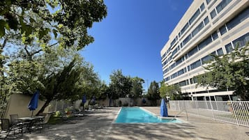 A pool area with lounge chairs and umbrellas, surrounded by trees and a building.