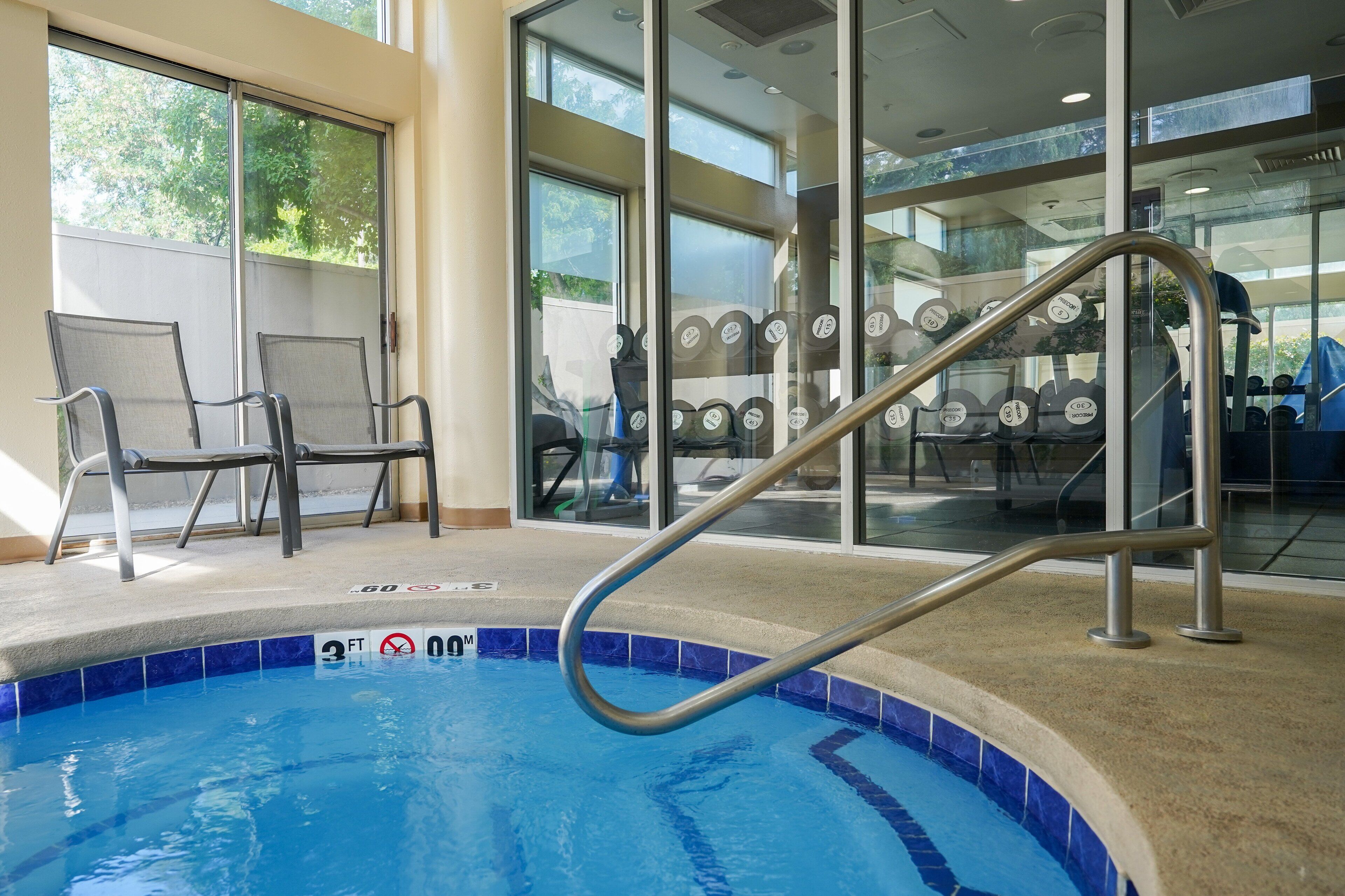 An indoor swimming pool with a metal ladder, lounge chairs, and exercise equipment.