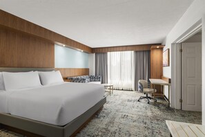 Una habitación de hotel con una cama grande, un escritorio, una silla y una ventana con cortinas.