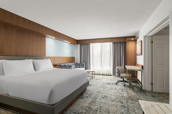 Een hotelkamer met een groot bed, een bureau, een stoel en een raam met gordijnen.