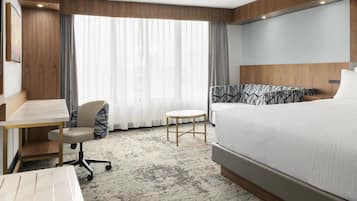 A hotel room with a bed, a desk, a chair, and a small table.